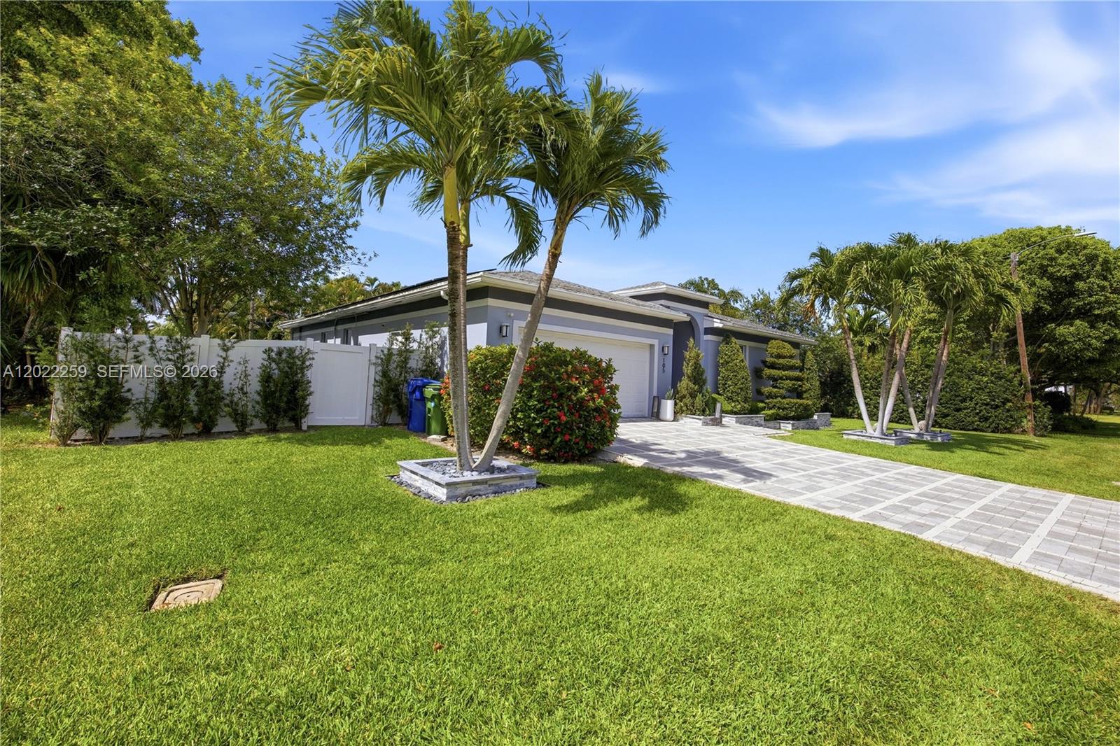 A single-story house with a paved driveway, palm trees, and a white privacy fence — 105 NE 28th Ct, Wilton Manors FL 33334, WILTON MANORS, FL