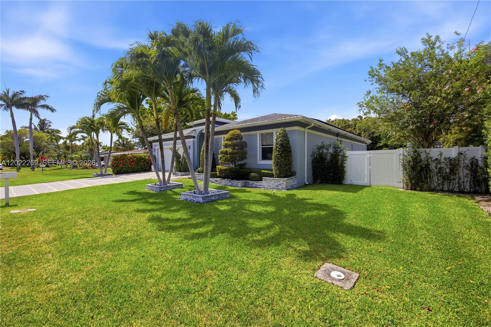 A single-story house with a gray exterior, palm trees, and a white vinyl fence — 105 NE 28th Ct, Wilton Manors FL 33334, WILTON MANORS, FL