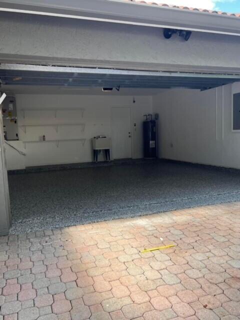 A garage with a gray speckled epoxy floor, white walls, shelving, and a water heater — 10330 Copper Lake Drive, Boynton Beach FL 33437, BOYNTON BEACH, FL