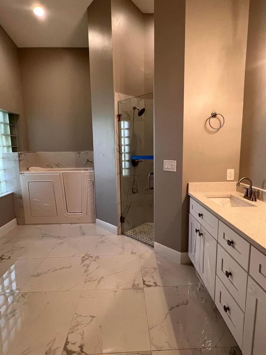 A bathroom features a walk-in tub, a glass-enclosed shower, and a white vanity with marble-look flooring — 10330 Copper Lake Drive, Boynton Beach FL 33437, BOYNTON BEACH, FL