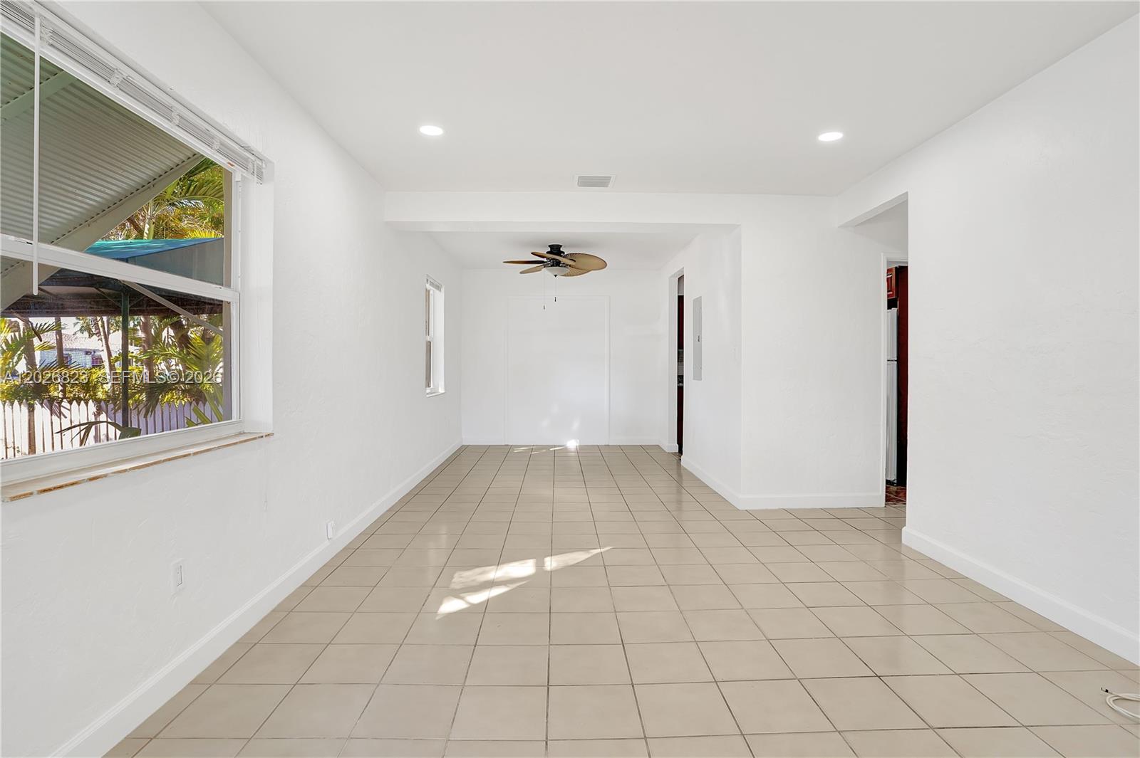 An empty room features white walls, tan tile flooring, a ceiling fan, and a large window — 5985 SW 41st St, Miami FL 33155, MIAMI, FL