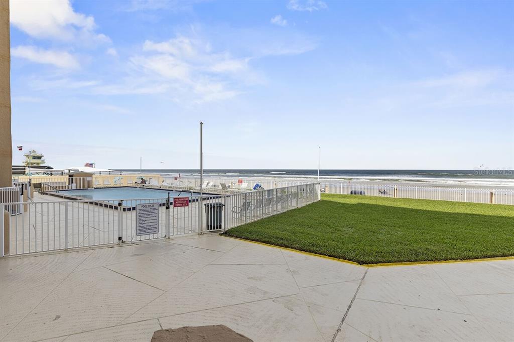 A swimming pool sits on a patio next to a grassy lawn overlooking the ocean — 421 S ATLANTIC AVENUE UNIT 103, NEW SMYRNA BEACH, FL