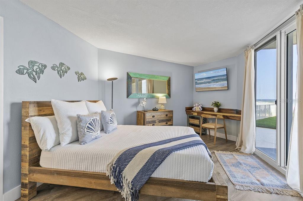 A bedroom with a wooden bed frame, desk, and sliding glass doors overlooking the ocean — 421 S ATLANTIC AVENUE UNIT 103, NEW SMYRNA BEACH, FL