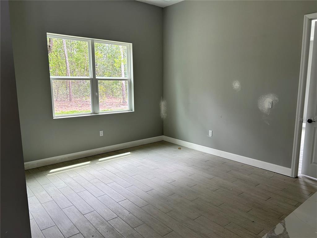 An empty room features gray walls, light wood-look tile flooring, and a window overlooking trees — 2628 W SCILLA DRIVE, DUNNELLON, FL
