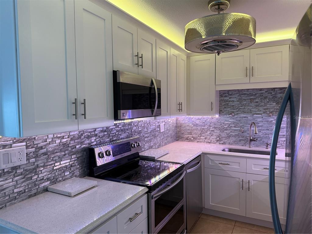 A kitchen features white cabinets, stainless steel appliances, a stone tile backsplash, and under-cabinet lighting — 21300 BRINSON AVENUE UNIT 101, PORT CHARLOTTE, FL