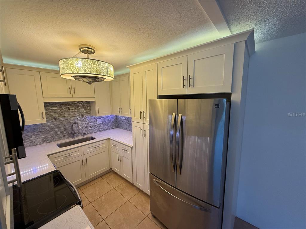 A kitchen features white cabinets, stainless steel appliances, a tiled backsplash, and a pendant light — 21300 BRINSON AVENUE UNIT 101, PORT CHARLOTTE, FL