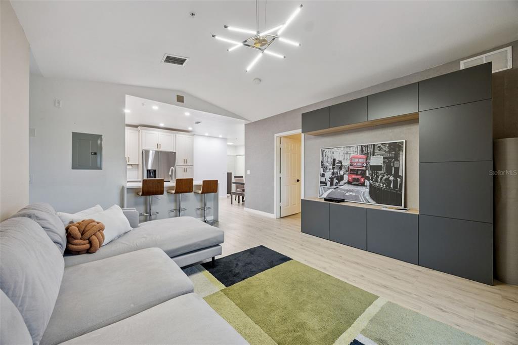 A modern living room features a grey sectional sofa, a large media wall, and kitchen seating — 5550 E MICHIGAN STREET UNIT 2321, ORLANDO, FL