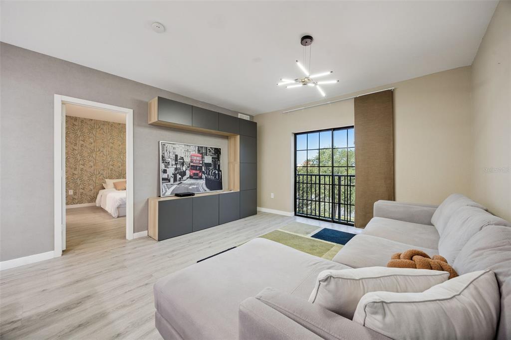 A living room features light wood flooring, a grey sectional sofa, and a wall-mounted entertainment unit — 5550 E MICHIGAN STREET UNIT 2321, ORLANDO, FL