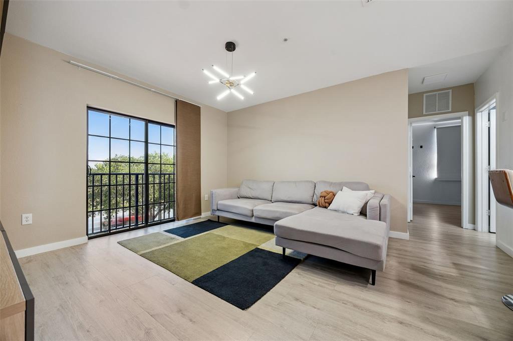 A living room features light wood floors, a gray sectional sofa, and a sliding glass door — 5550 E MICHIGAN STREET UNIT 2321, ORLANDO, FL