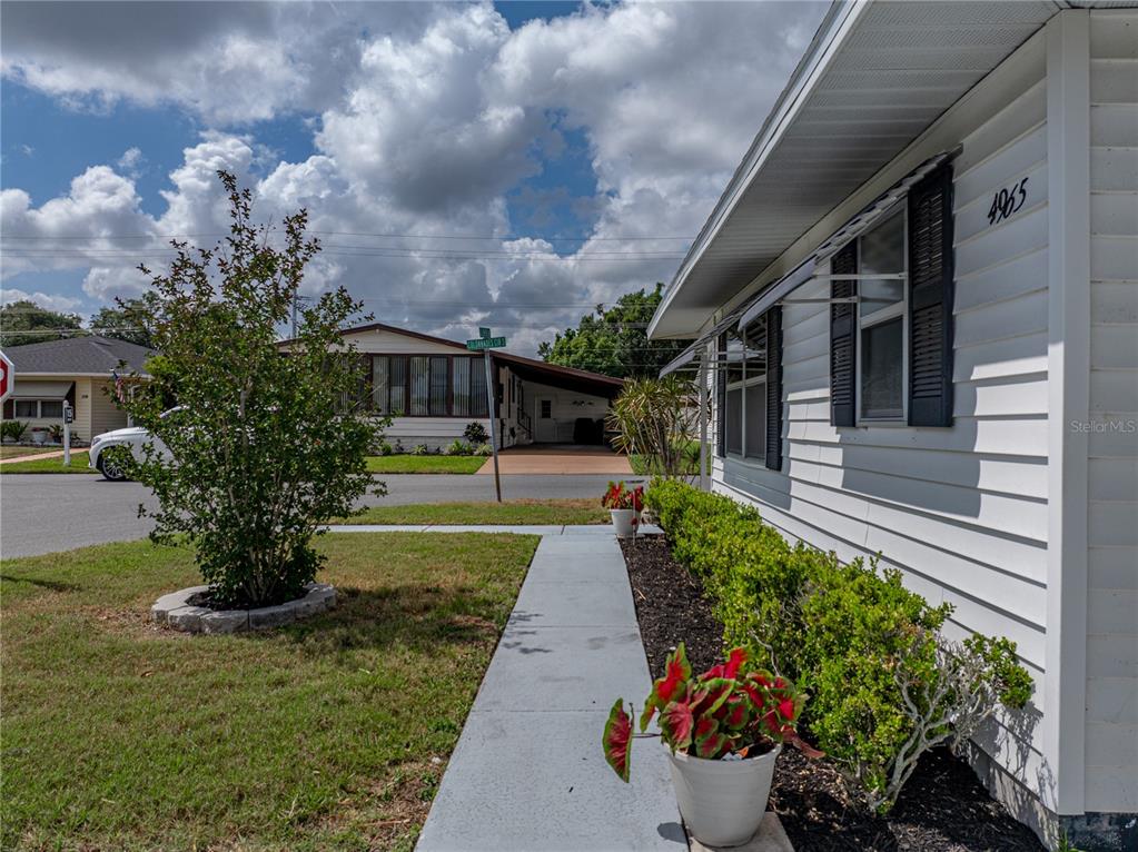 A white house exterior features a concrete walkway, landscaped bushes, and potted plants — 4965 GOLDENVIEW LANE, LAKELAND, FL