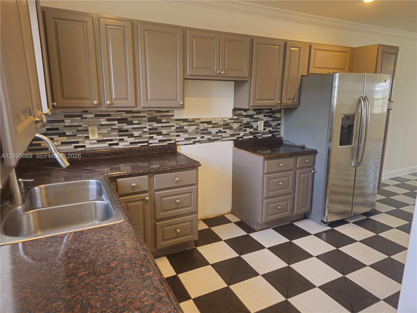 A kitchen features brown cabinets, granite countertops, a mosaic backsplash, and black-and-white checkered flooring — 2521 NW 13th Ave # 2521, Miami FL 33142, MIAMI, FL
