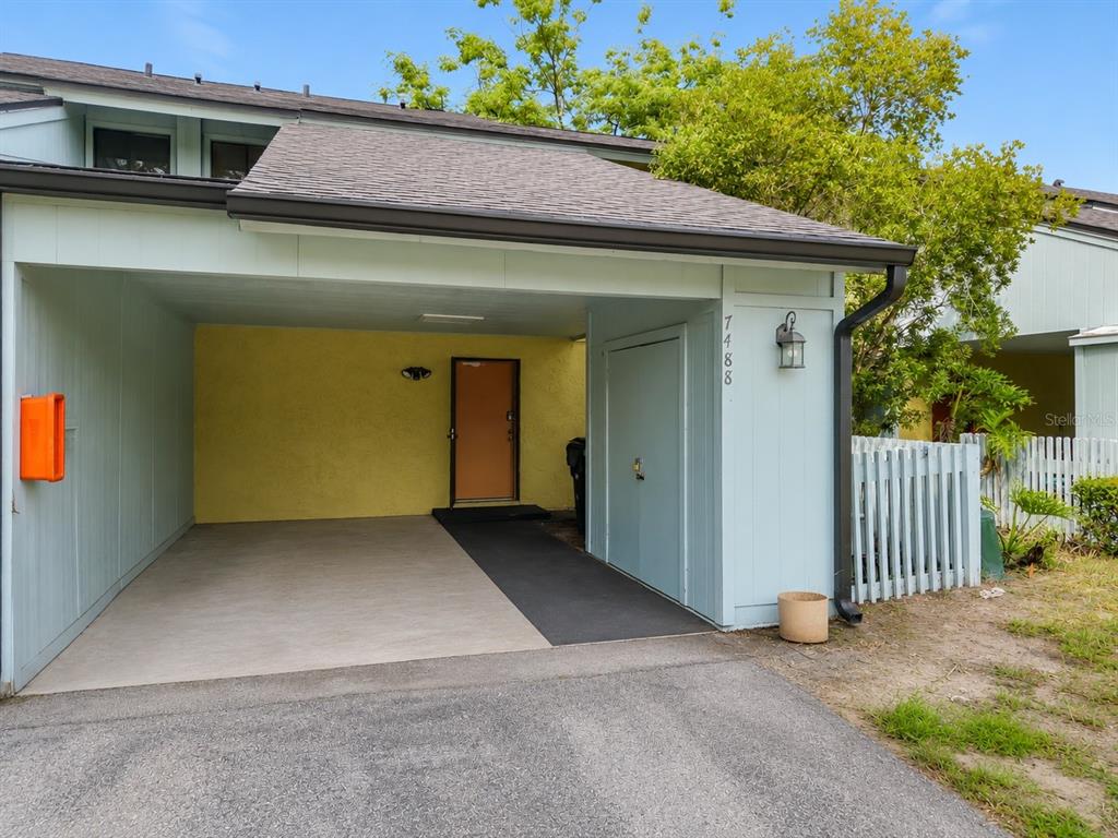 A covered carport leads to a front door with a yellow wall and light blue siding — 7488 WHISPERWOOD DRIVE UNIT 28, WINTER PARK, FL