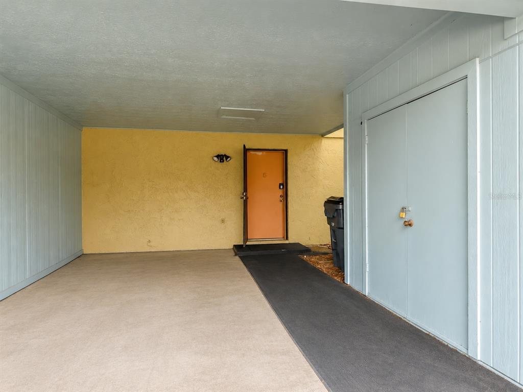 A covered carport features a yellow wall, an orange front door, and a storage closet — 7488 WHISPERWOOD DRIVE UNIT 28, WINTER PARK, FL