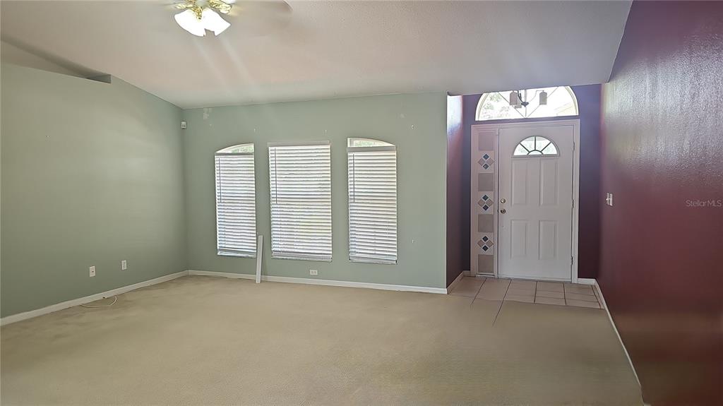 A living room features light green walls, a vaulted ceiling, carpeted flooring, and a front door — 4030 LAKE BLUFF DRIVE, MASCOTTE, FL