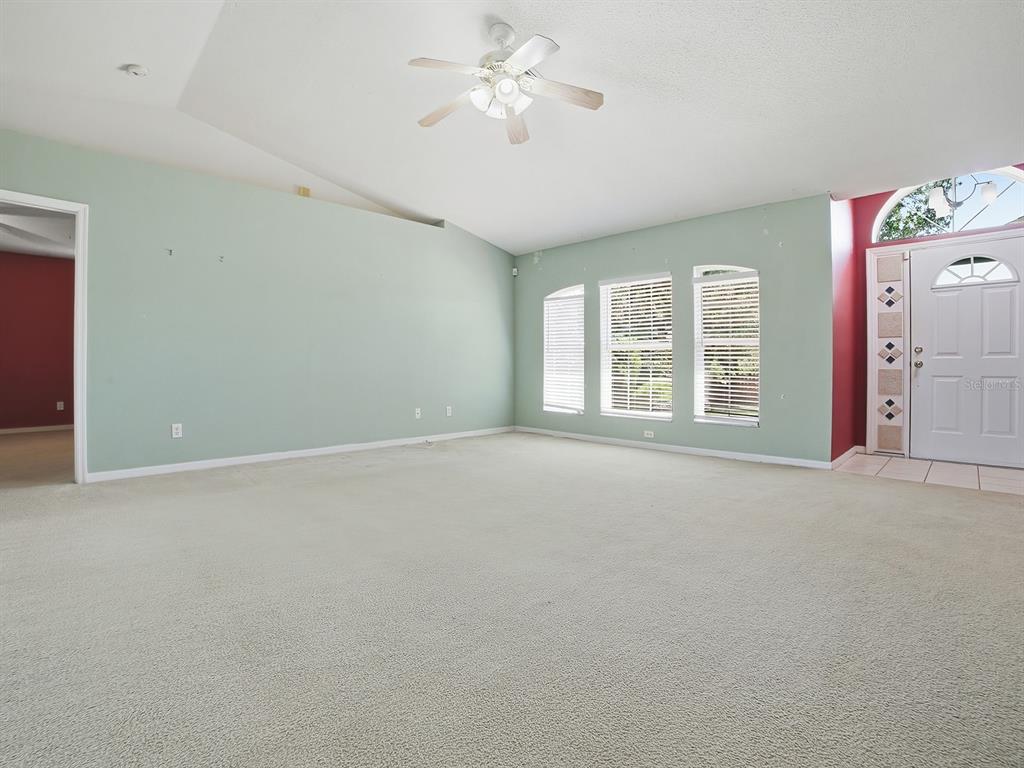 An empty living room with light green walls, beige carpet, and a ceiling fan — 4030 LAKE BLUFF DRIVE, MASCOTTE, FL