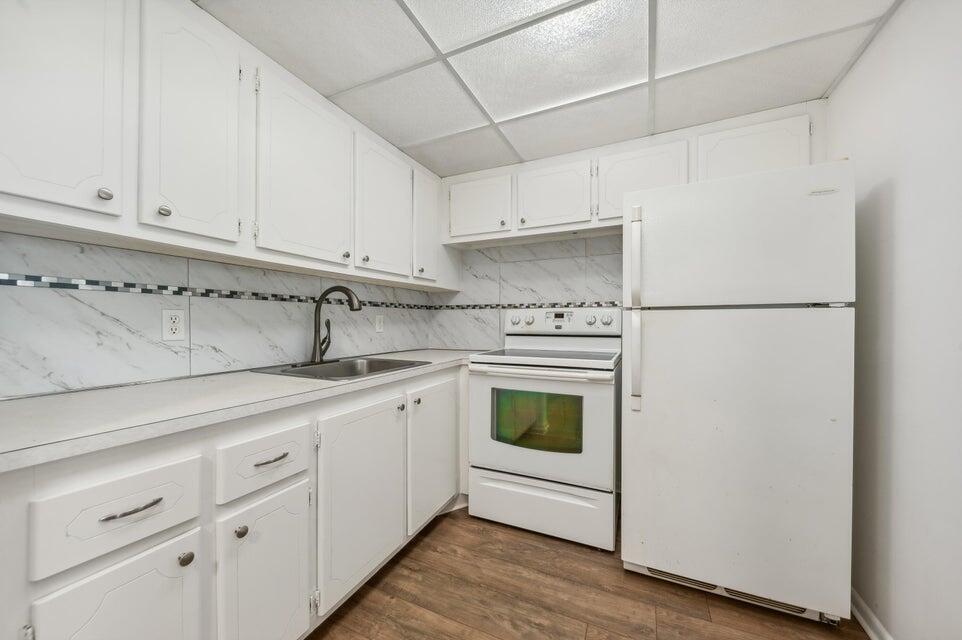 A white kitchen features marble-look backsplash tile, white cabinets, a stove, and a refrigerator — 98 Ventnor E # 98, Deerfield Beach FL 33442, DEERFIELD BEACH, FL