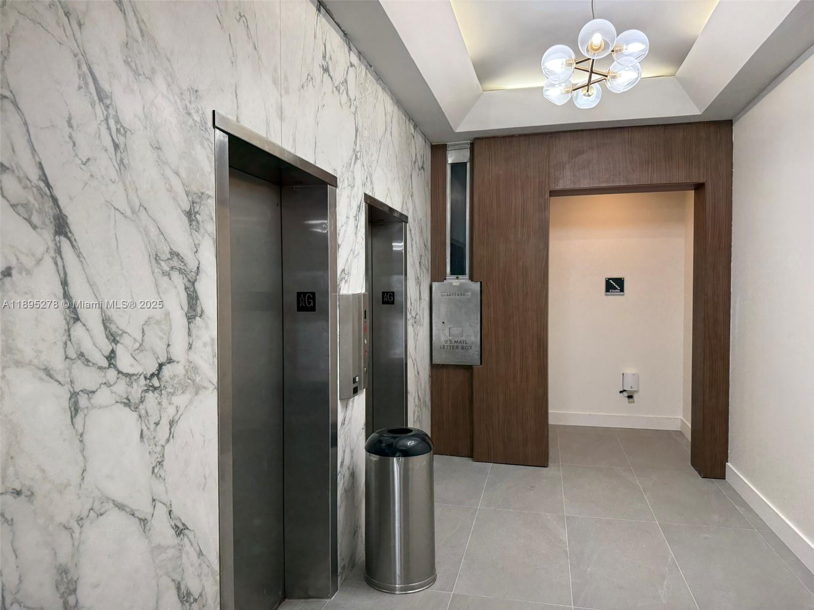 An elevator lobby features marble walls, stainless steel doors, a metal trash can, and wood paneling — 299 Alhambra Cir, Coral Gables FL 33134, CORAL GABLES, FL