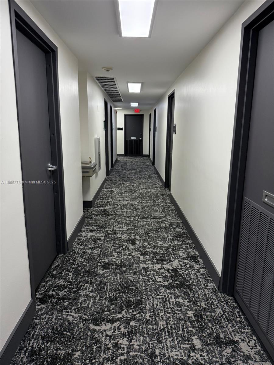 A long, narrow hallway features gray doors, white walls, and patterned gray carpet — 299 Alhambra Cir, Coral Gables FL 33134, CORAL GABLES, FL