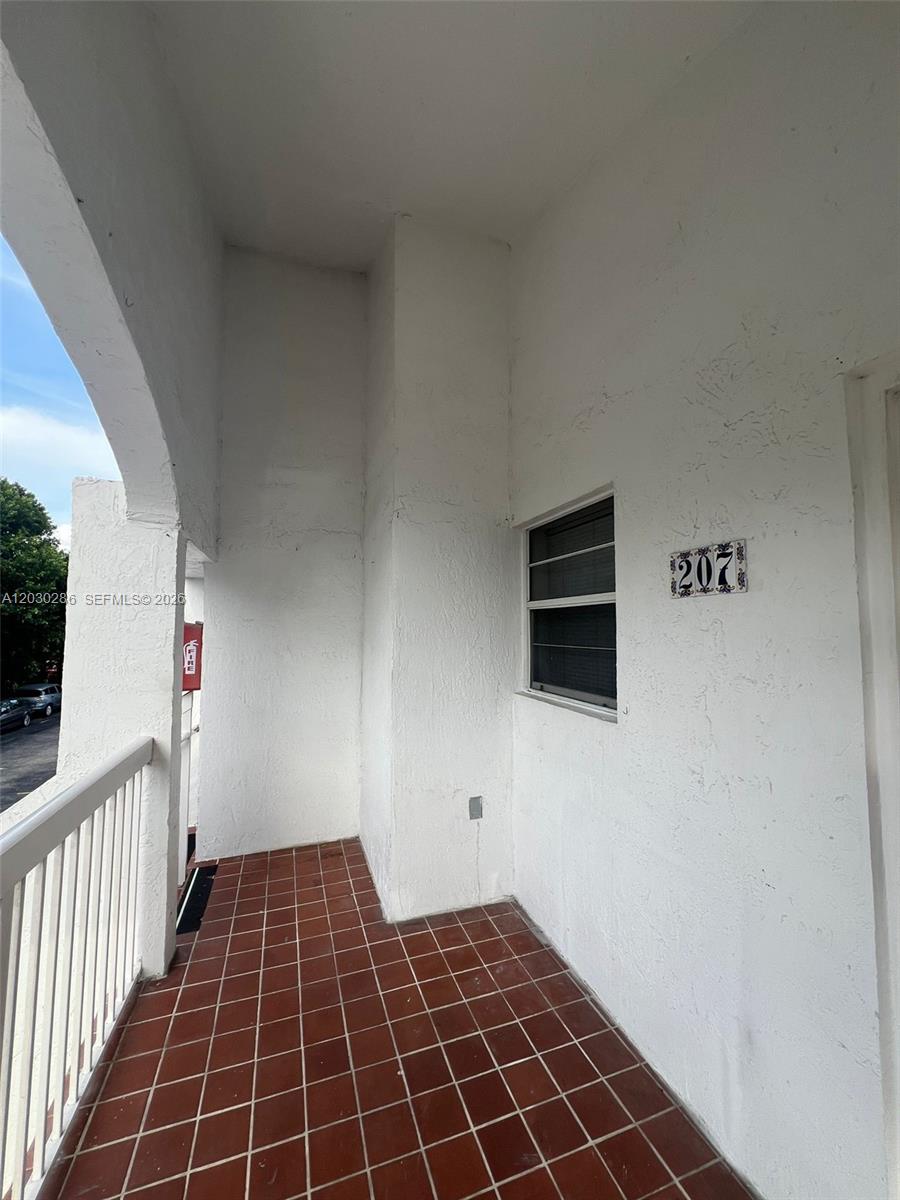 A covered balcony features red tile flooring, white walls, and a unit number 207 sign — 15315 SW 76th Ter # 207, Miami FL 33193, MIAMI, FL
