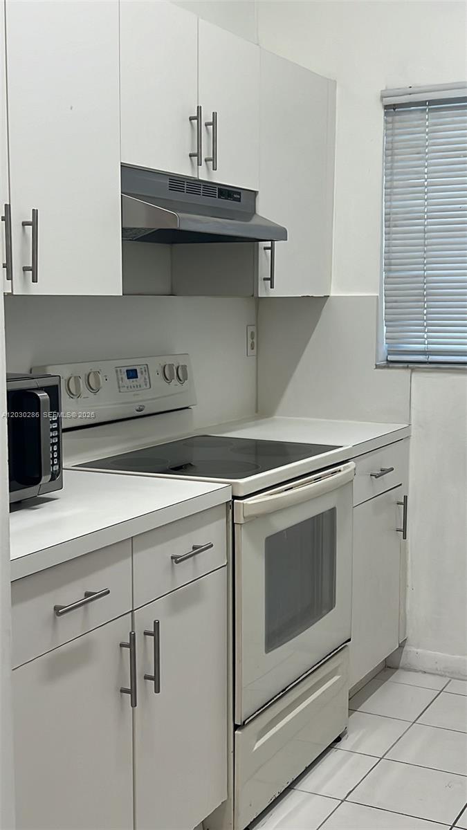 A kitchen features white cabinets, a glass-top stove, a range hood, and tiled flooring — 15315 SW 76th Ter # 207, Miami FL 33193, MIAMI, FL
