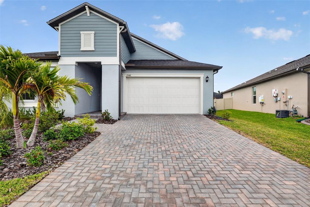 A single-story house with blue siding, a white garage door, and a brick paver driveway — 7542 117TH LANE E, PALMETTO, FL