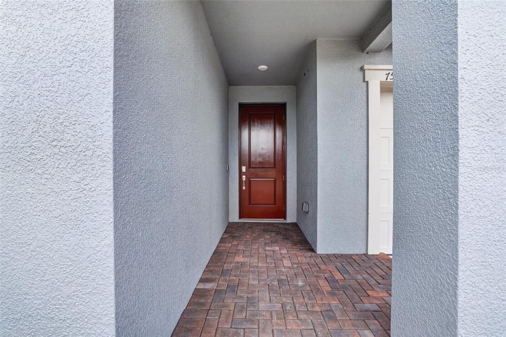 A covered entryway features a dark wood front door and a brick paver floor — 7542 117TH LANE E, PALMETTO, FL