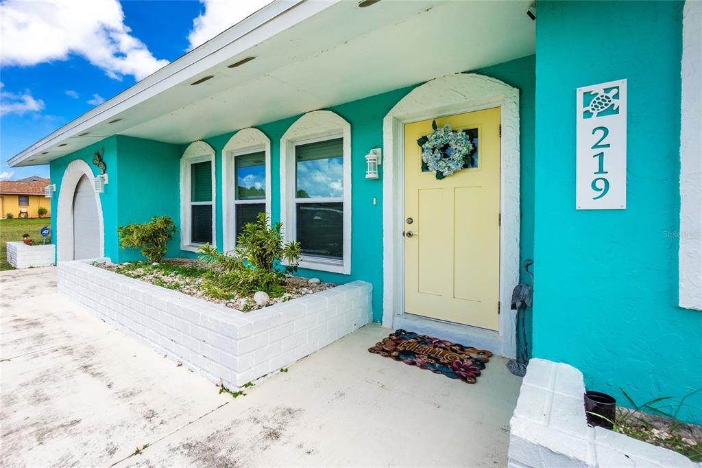 The exterior of a turquoise house features a yellow front door and a brick planter — 219 CADDY ROAD, ROTONDA WEST, FL