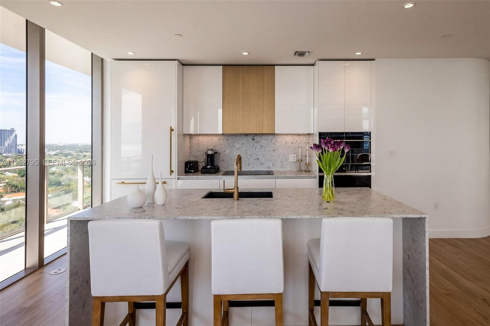 A modern kitchen features a stone island, white cabinetry, wood accents, and floor-to-ceiling windows — 2678 Tigertail Ave # 1707, Miami FL 33133, MIAMI, FL