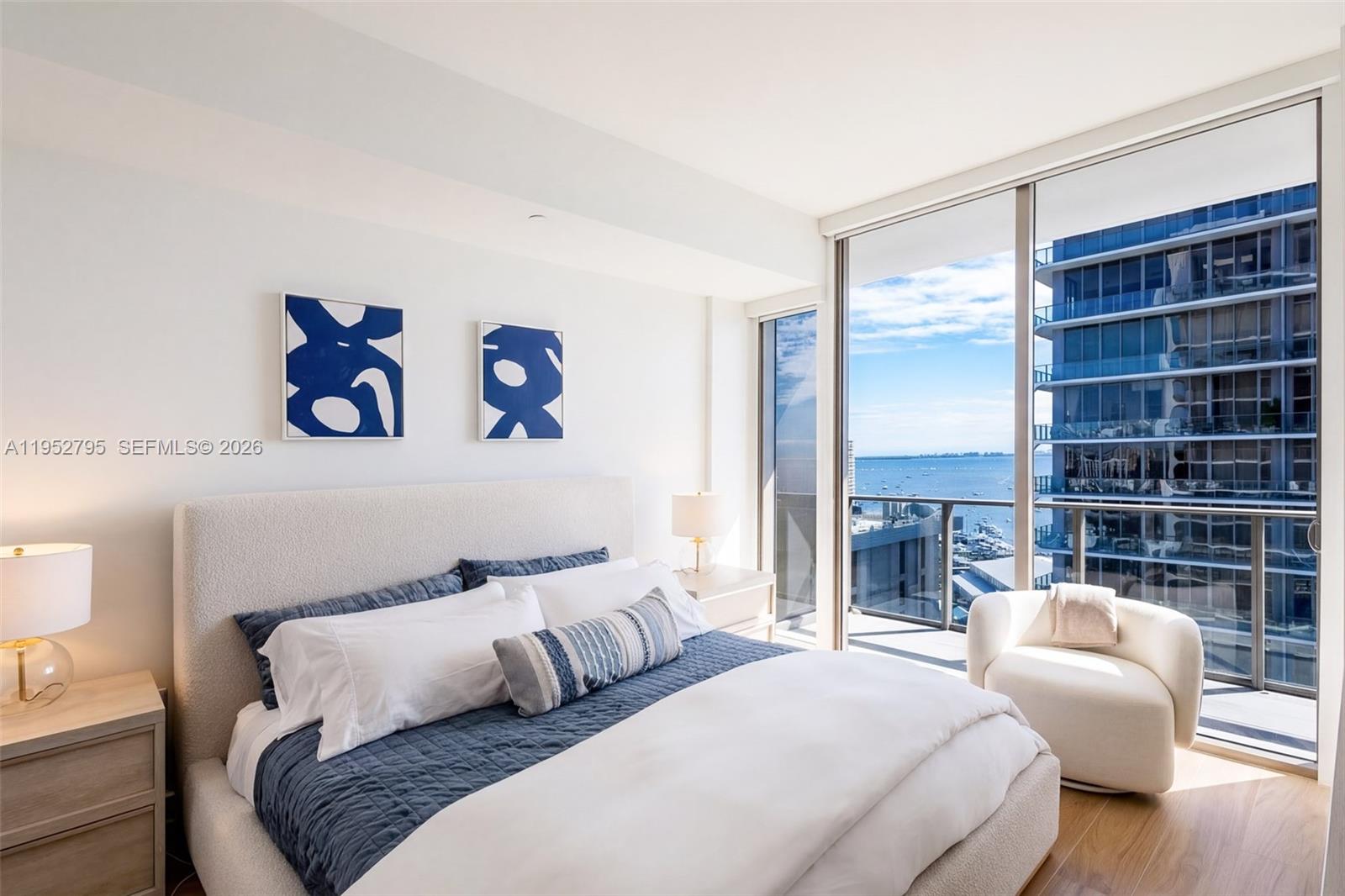 A bedroom features a bed with blue bedding, two abstract paintings, and a balcony view — 2678 Tigertail Ave # 1707, Miami FL 33133, MIAMI, FL