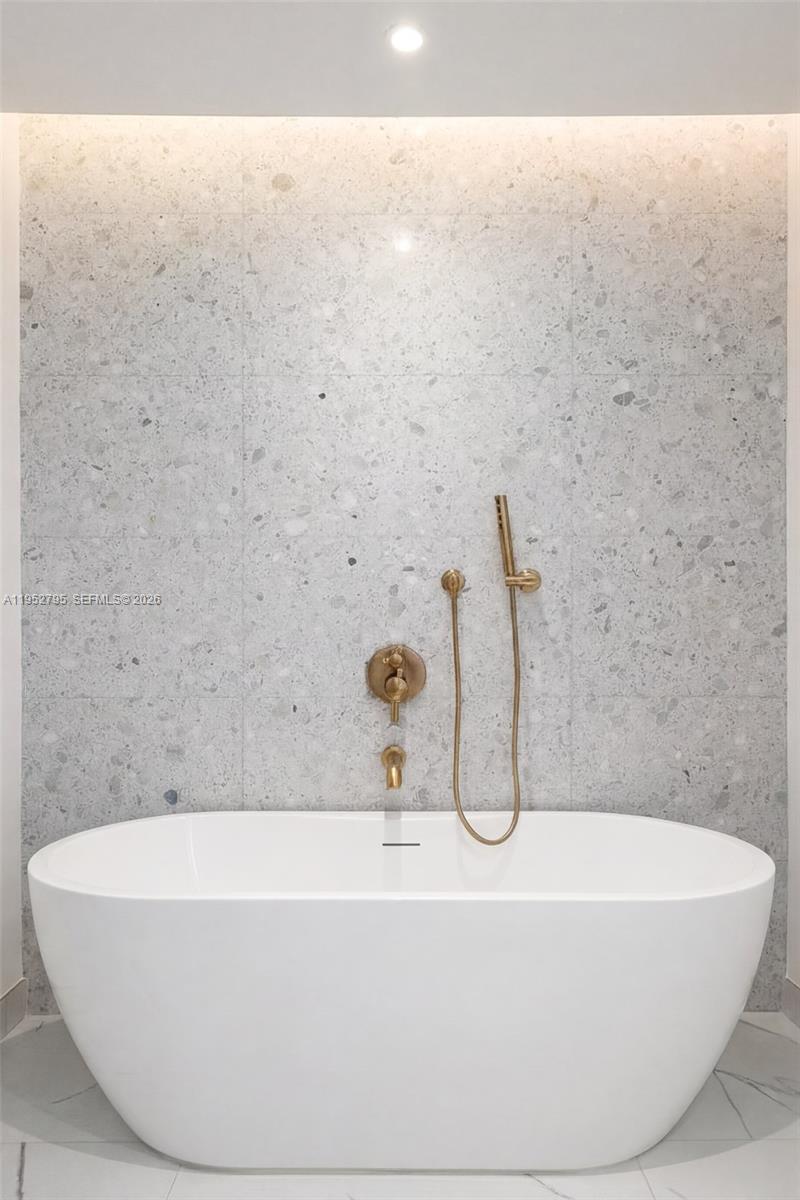 A white freestanding bathtub sits against a wall with gray terrazzo-style tile and gold fixtures — 2678 Tigertail Ave # 1707, Miami FL 33133, MIAMI, FL
