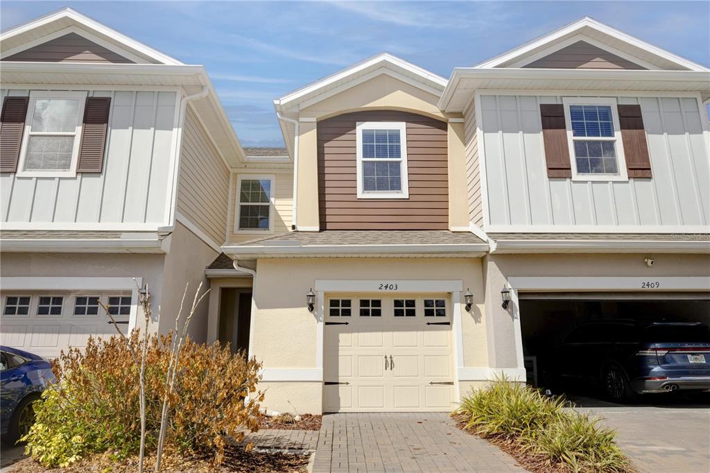 A three-unit townhouse complex features beige stucco, vertical siding, and individual garage doors — 2403 SEDGE GRASS WAY, ORLANDO, FL