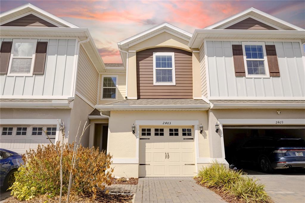 A three-unit townhouse exterior features beige stucco, white vertical siding, and a paved driveway — 2403 SEDGE GRASS WAY, ORLANDO, FL