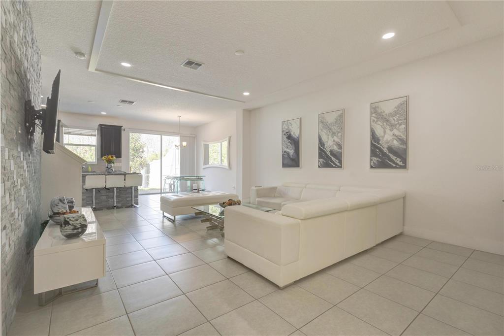 A modern living room features white tile floors, a white sectional sofa, and stone accents — 2403 SEDGE GRASS WAY, ORLANDO, FL