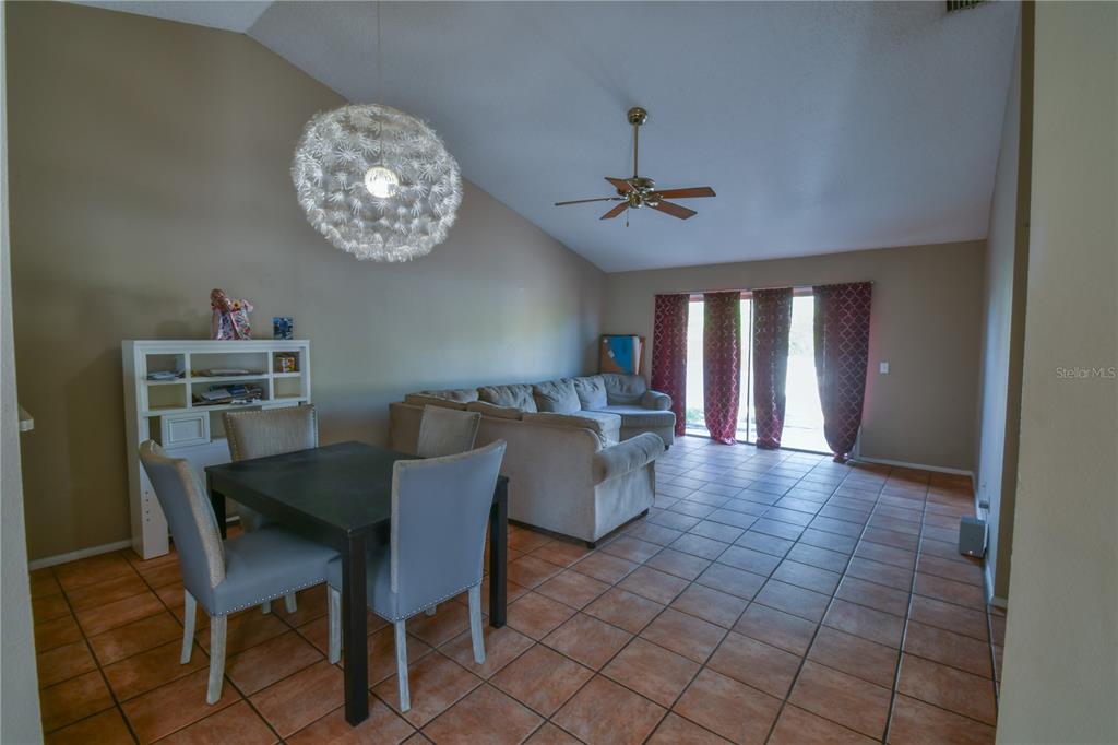 An open-concept living area features tan tile flooring, a vaulted ceiling, and a sliding glass door — 7416 LITTLE POND COURT, ORLANDO, FL