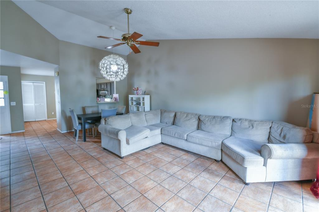A spacious room features tan tile flooring, a vaulted ceiling, and a large dandelion-style chandelier — 7416 LITTLE POND COURT, ORLANDO, FL
