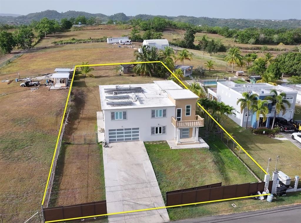 An aerial view shows a two-story house with solar panels on a fenced residential lot — SR 308 km 5.8 INT SOLAR MIRADERO LOT # 2, CABO ROJO, PR