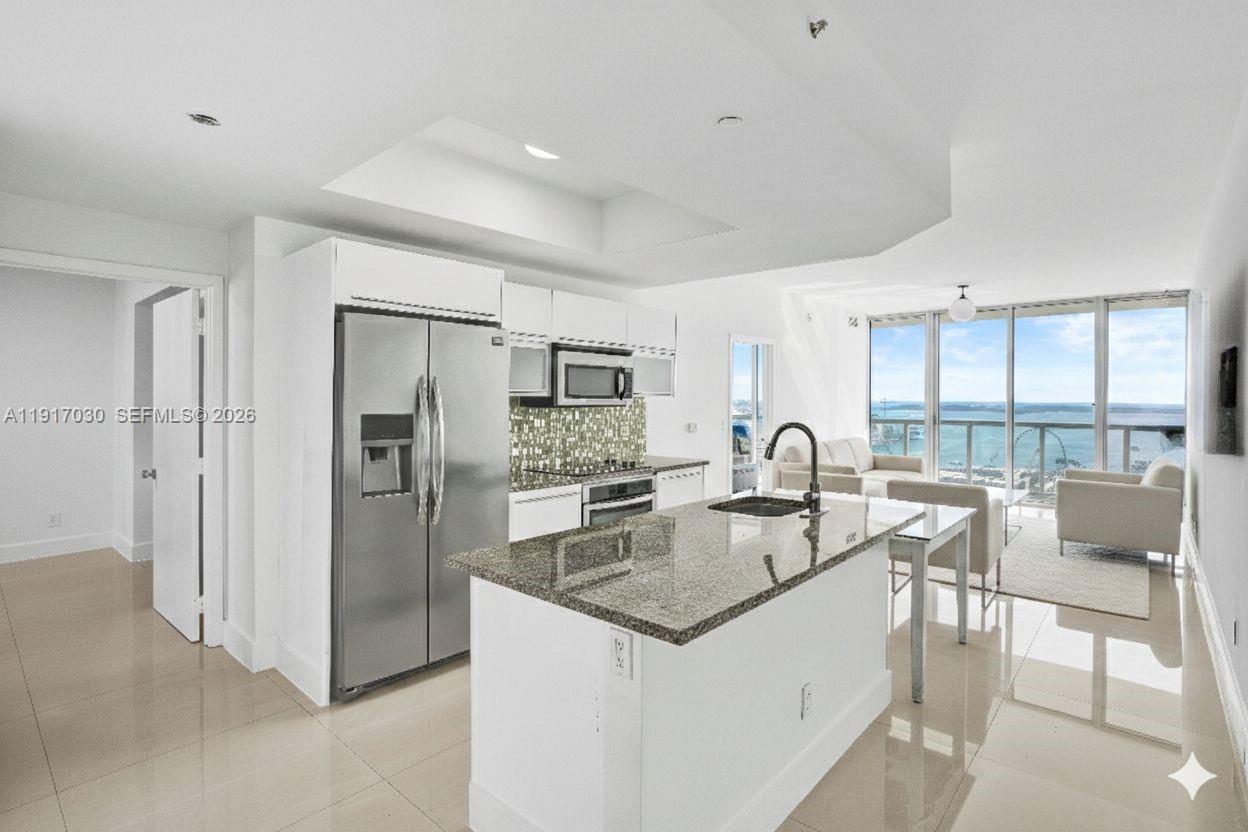 A modern bedroom features a bed, white tile floors, and floor-to-ceiling windows overlooking a harbor — 888 Biscayne Blvd # 2904, Miami FL 33132, MIAMI, FL
