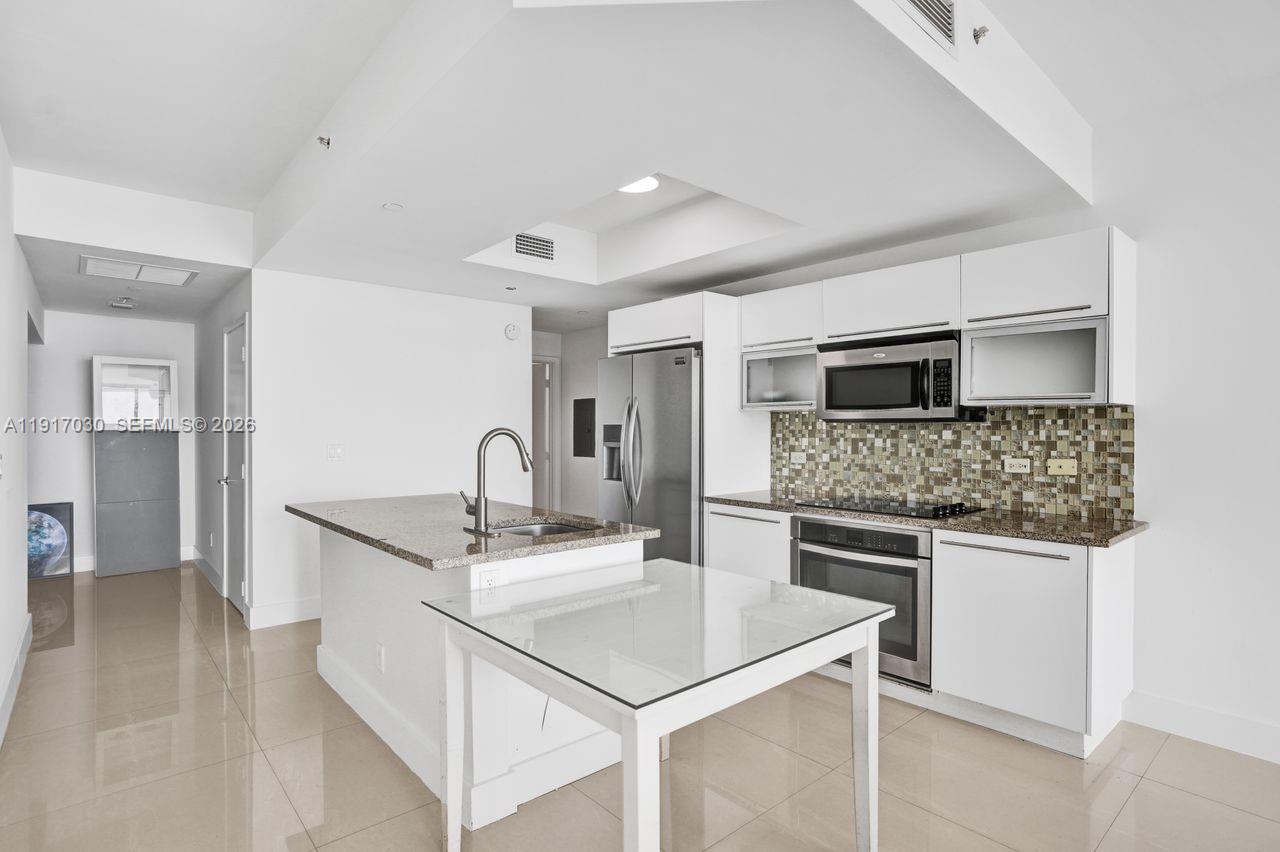 A modern kitchen with granite countertops and stainless steel appliances overlooks a bright living area — 888 Biscayne Blvd # 2904, Miami FL 33132, MIAMI, FL