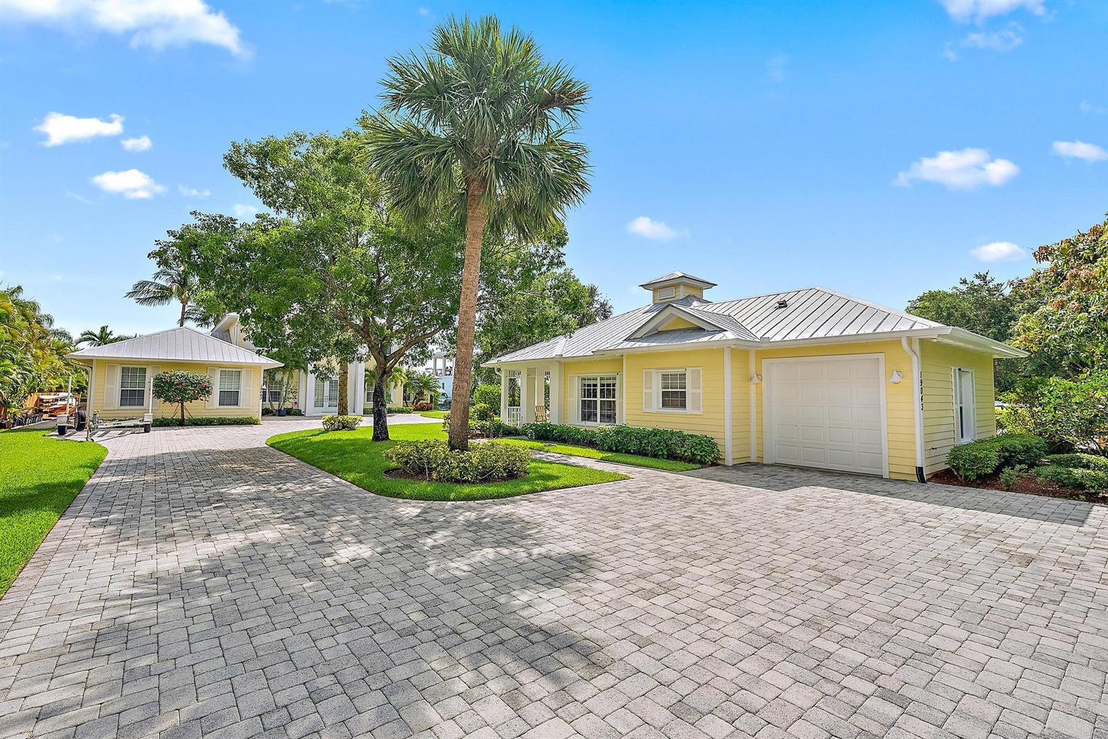 A yellow house with a metal roof and a paved driveway sits under a palm tree — 19043 SE Jupiter River Drive, Jupiter FL 33458, JUPITER, FL