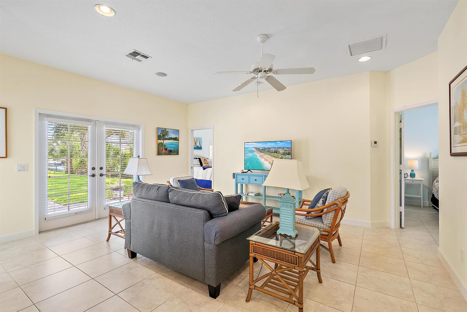 A living room with tile floors, a gray sofa, rattan chairs, and a ceiling fan — 19043 SE Jupiter River Drive, Jupiter FL 33458, JUPITER, FL