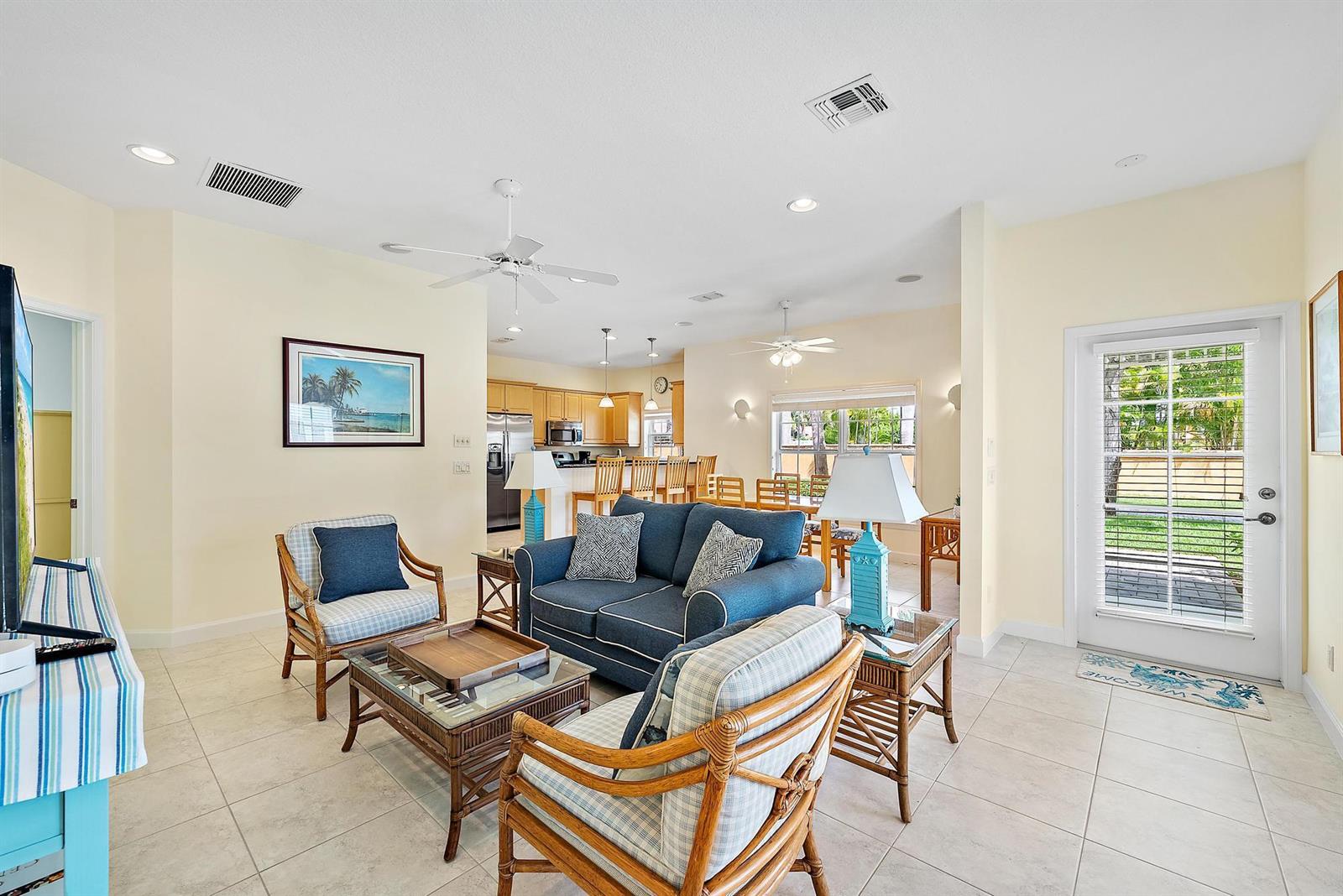A living room with tile floors, a blue sofa, and rattan chairs leads to a kitchen — 19043 SE Jupiter River Drive, Jupiter FL 33458, JUPITER, FL