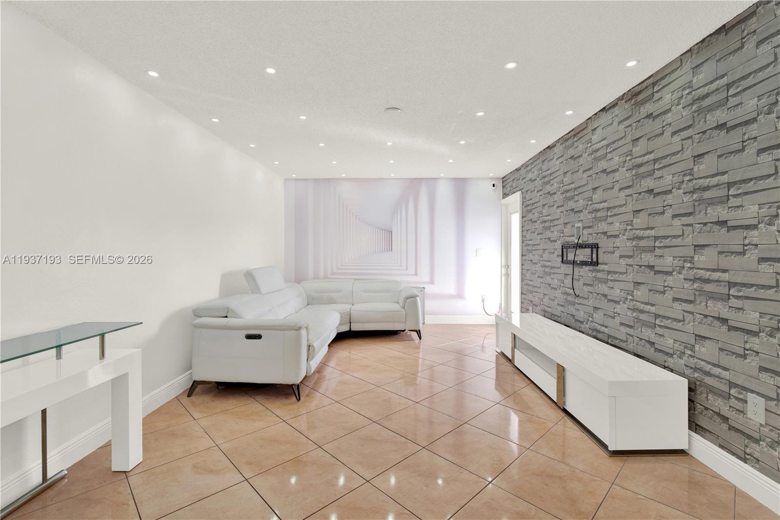 A living room features a white sectional sofa, a stone accent wall, and tiled floors — 5665 W 20th Ave # 415, Hialeah FL 33012, HIALEAH, FL