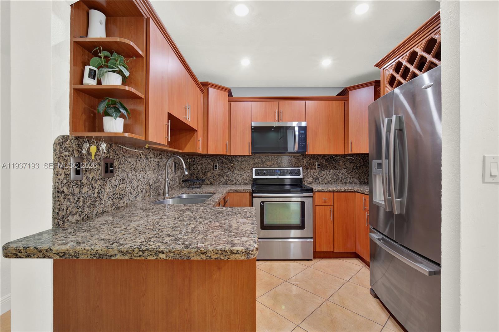 A kitchen features wood cabinets, granite countertops, stainless steel appliances, and tile flooring — 5665 W 20th Ave # 415, Hialeah FL 33012, HIALEAH, FL