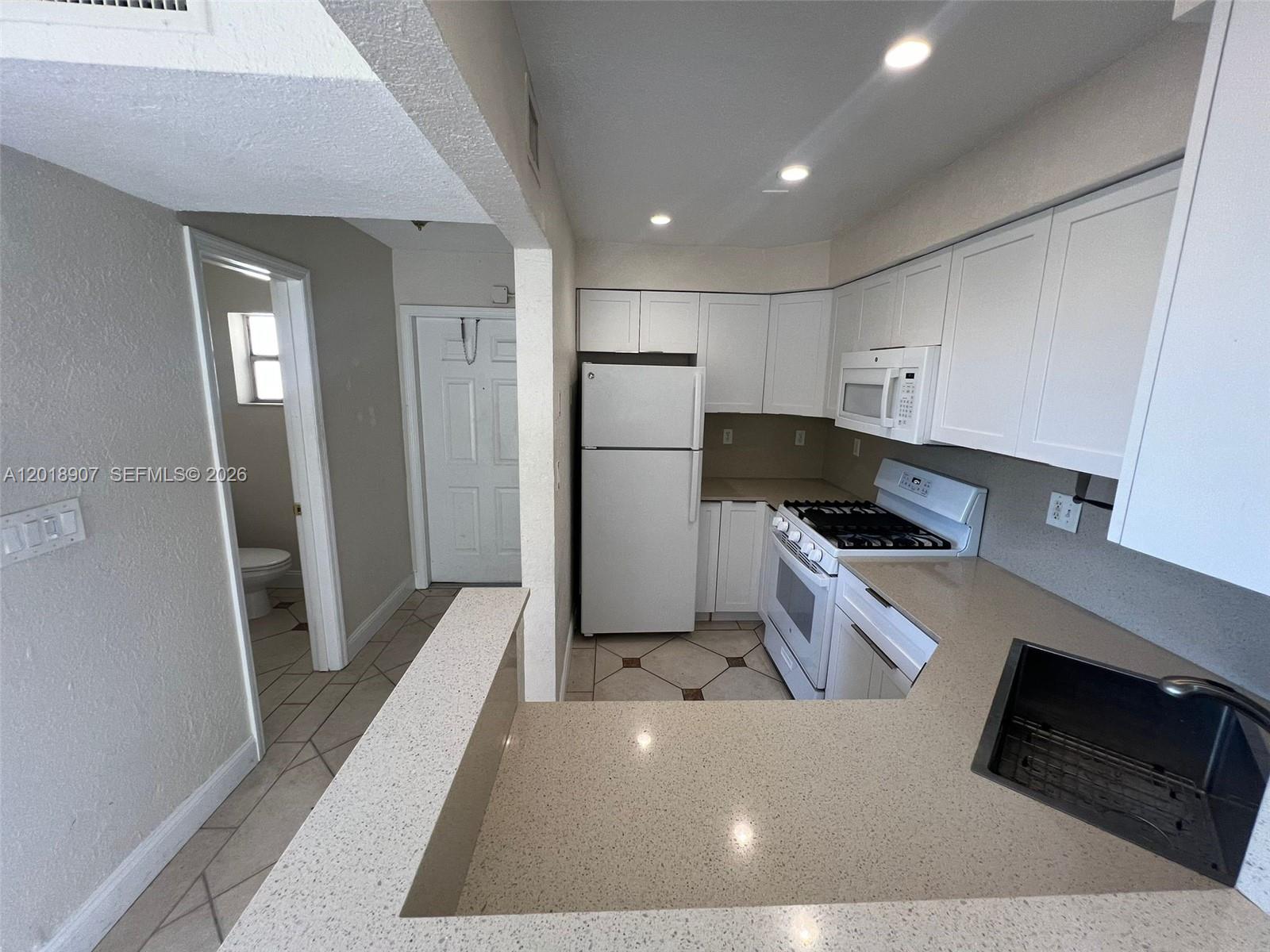 A kitchen features white cabinets, light countertops, a white refrigerator, and a tiled floor — 8600 SW 67th Ave # 938, Pinecrest FL 33156, PINECREST, FL
