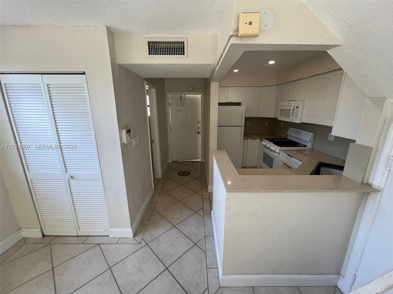 A kitchen with white cabinets and a breakfast bar opens into a tiled entryway — 8600 SW 67th Ave # 938, Pinecrest FL 33156, PINECREST, FL