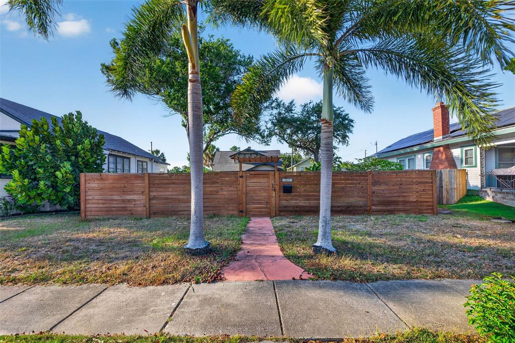 A wooden fence with a central gate stands in front of a house with palm trees — 2419 DARTMOUTH AVENUE N, ST PETERSBURG, FL