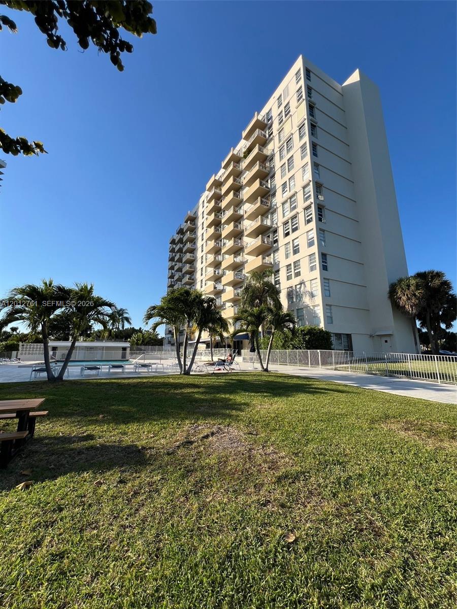 A tall residential building stands behind a grassy lawn with palm trees and a pool — 880 NE 69th St # 11M, Miami FL 33138, MIAMI, FL