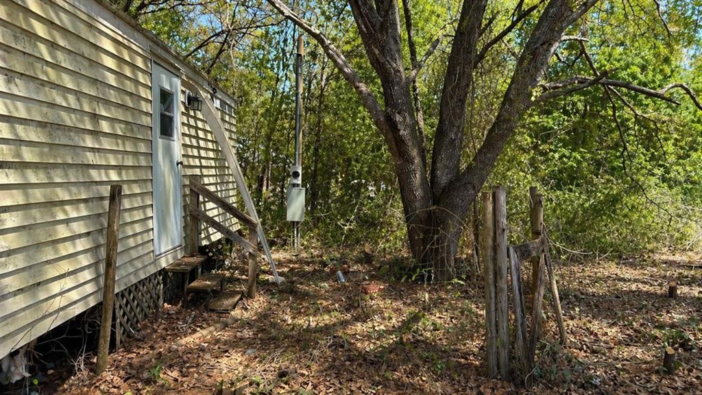 An exterior view of a mobile home with light siding, a wooden staircase, and surrounding trees — 11281 NE 64TH PLACE, WILLISTON, FL