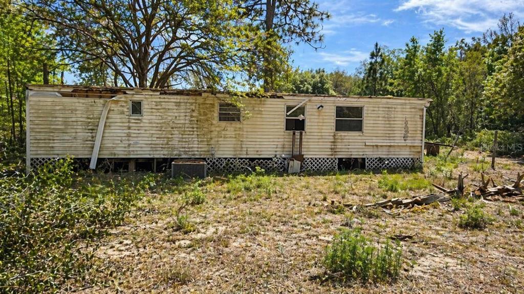 A weathered, single-wide mobile home with damaged roof trim sits on a wooded lot — 11281 NE 64TH PLACE, WILLISTON, FL