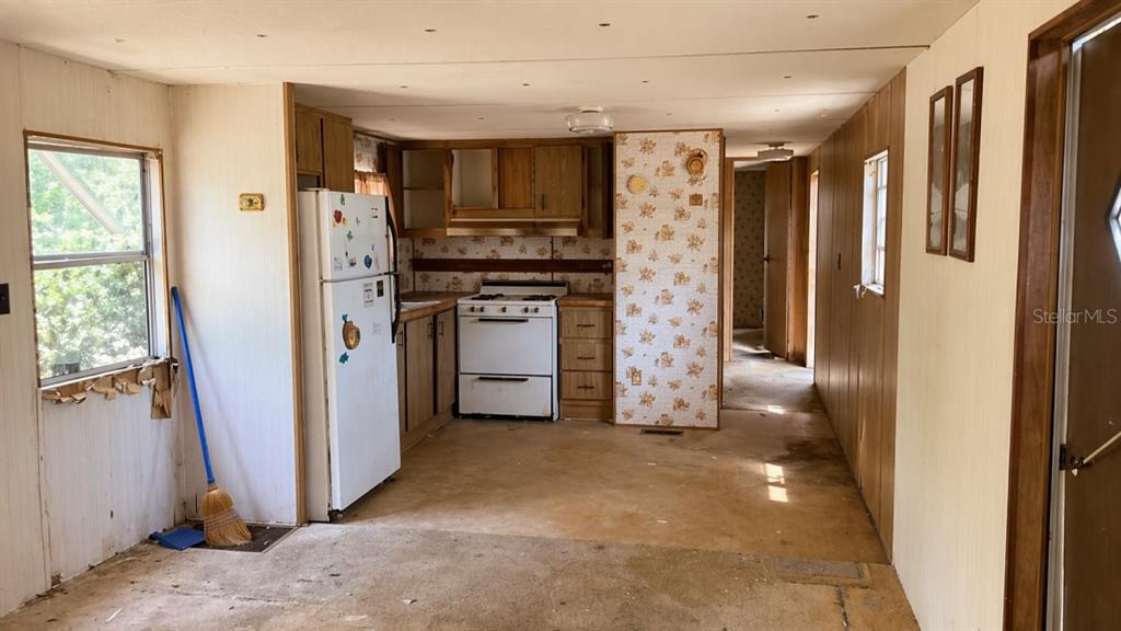 A kitchen with wood-paneled walls, floral wallpaper, and worn flooring in a mobile home — 11281 NE 64TH PLACE, WILLISTON, FL